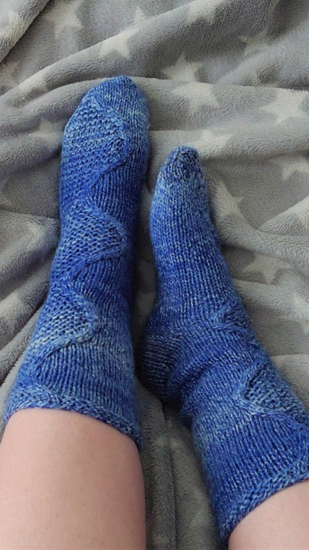 Tuonela River cable socks in blue, worn, on a grey star blanket